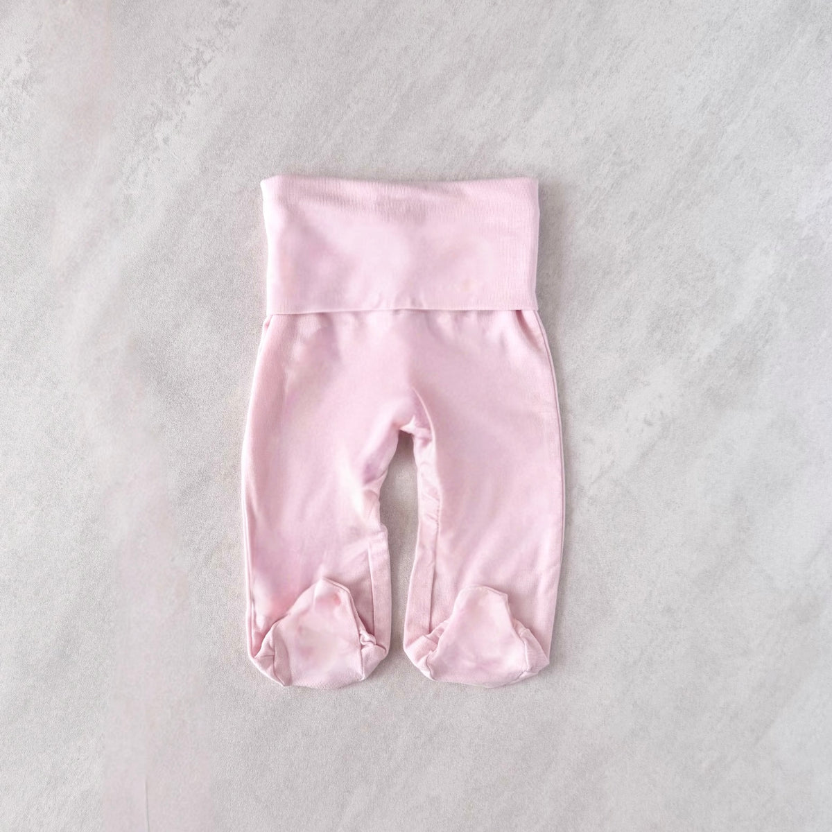 Pink tiny baby bottoms with footies on a light gray textured surface