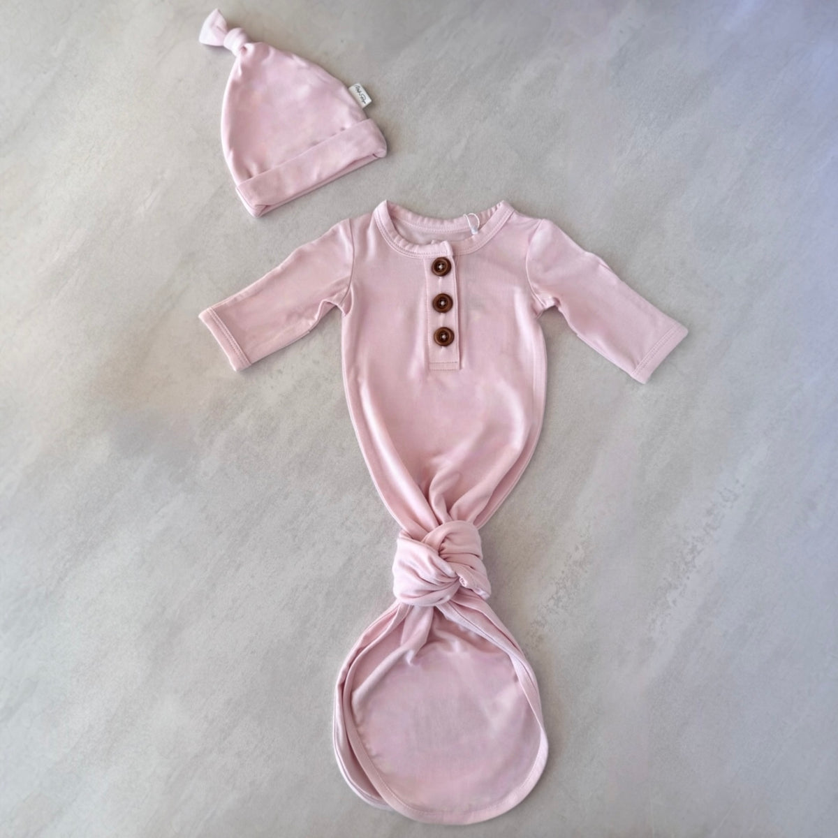 Pink premature baby outfit with long-sleeve top and knotted bottom on a light gray background