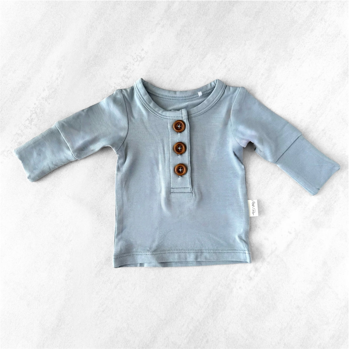 Light blue premature baby long-sleeve shirt with brown buttons on a white background