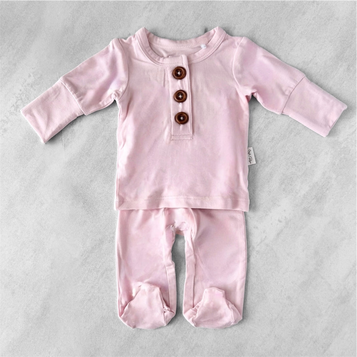 Pink preemie baby outfit with button details on a gray background